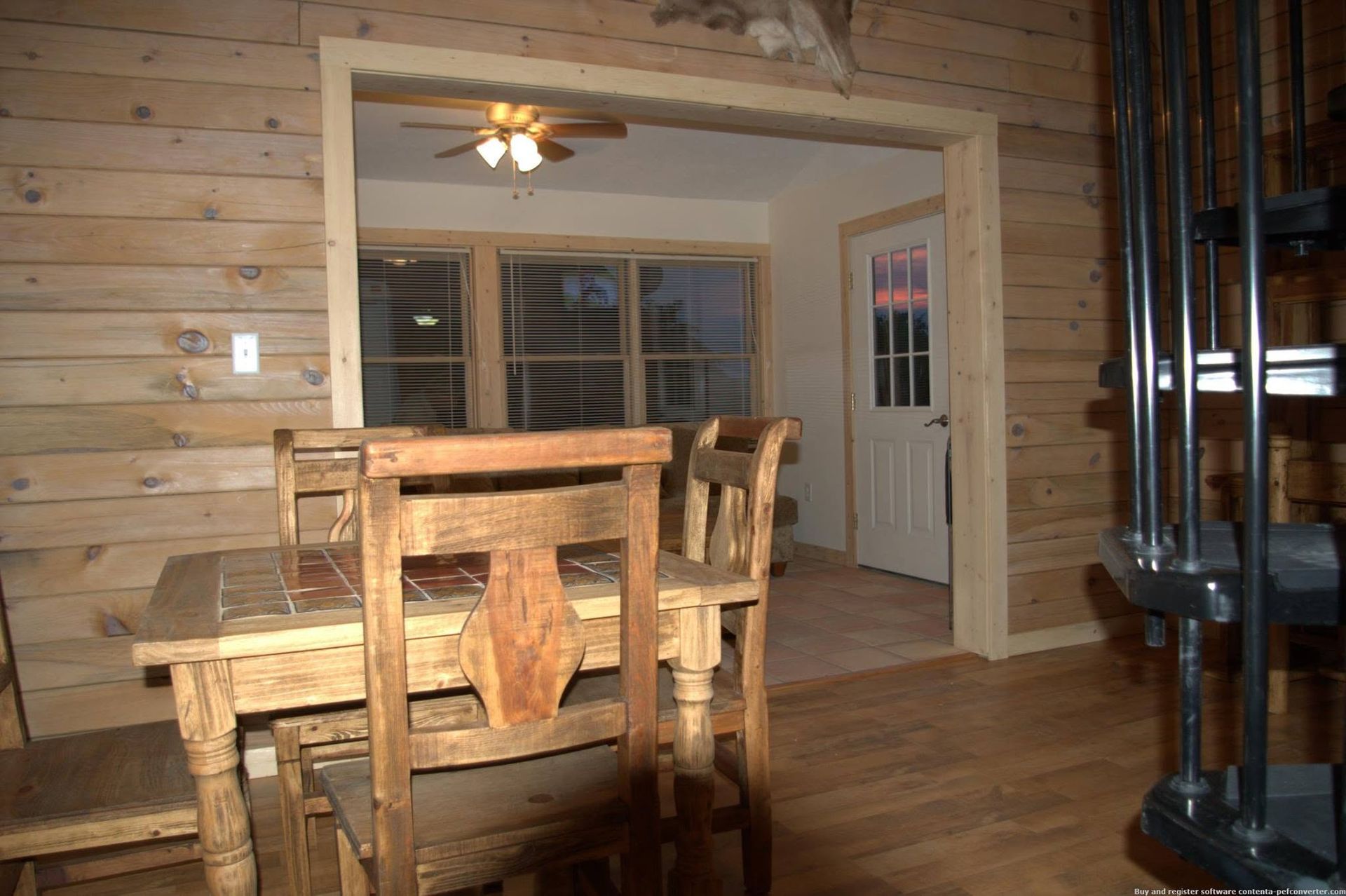Wood-paneled dining room with wooden table and chairs, ceiling fan, and tiled stove on the right