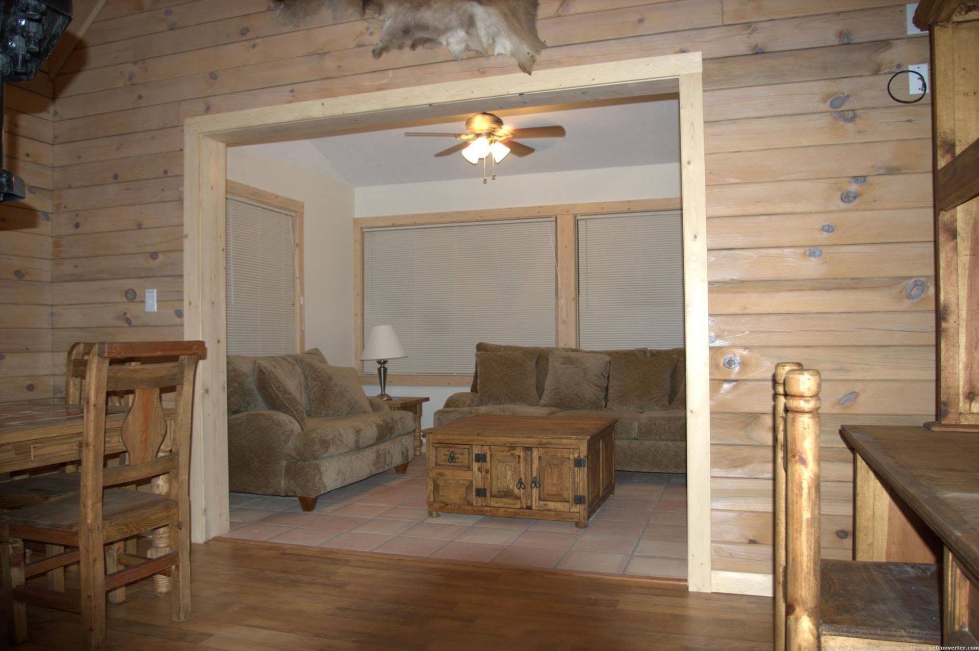 Wood-paneled cabin living room with tan sofas, coffee table, and ceiling fan