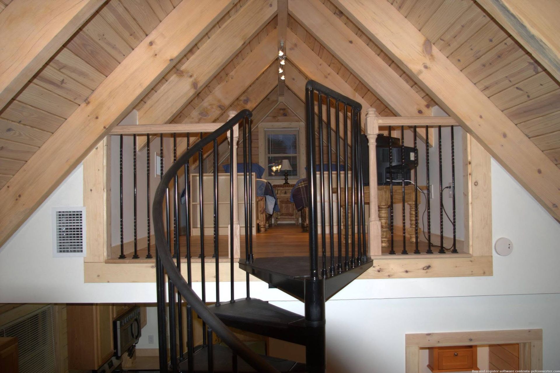 Loft spiral staircase centered in a wood-paneled attic room with vaulted ceiling.