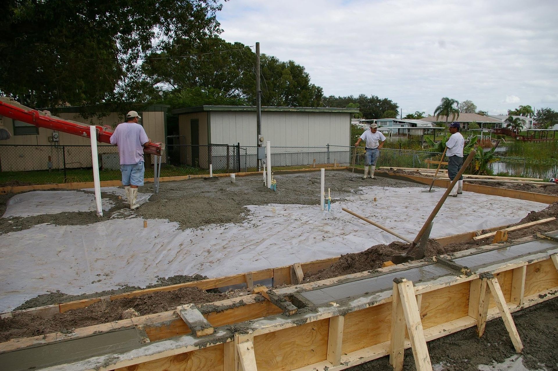 Construction site with workers pouring concrete for a foundation slab beside a small building