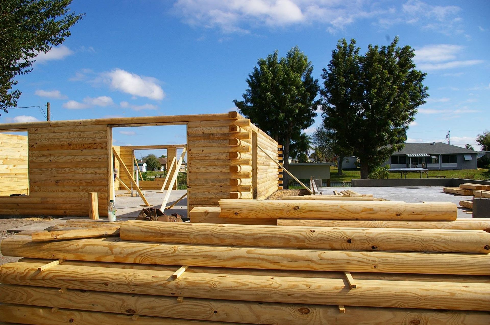 Log cabin under construction with stacked logs, wooden walls, and a bright blue sky.
