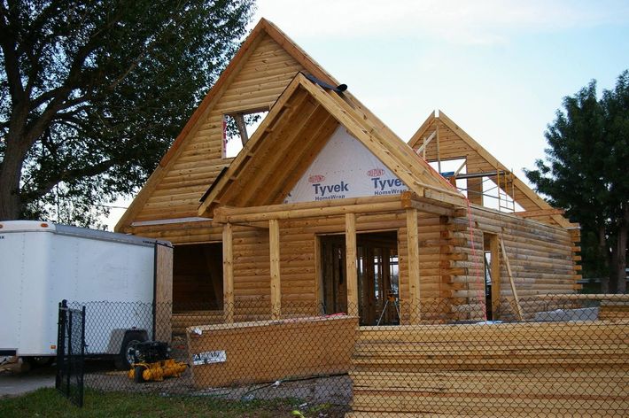 Partially built wooden house framed in lumber with a trailer beside it under a blue sky