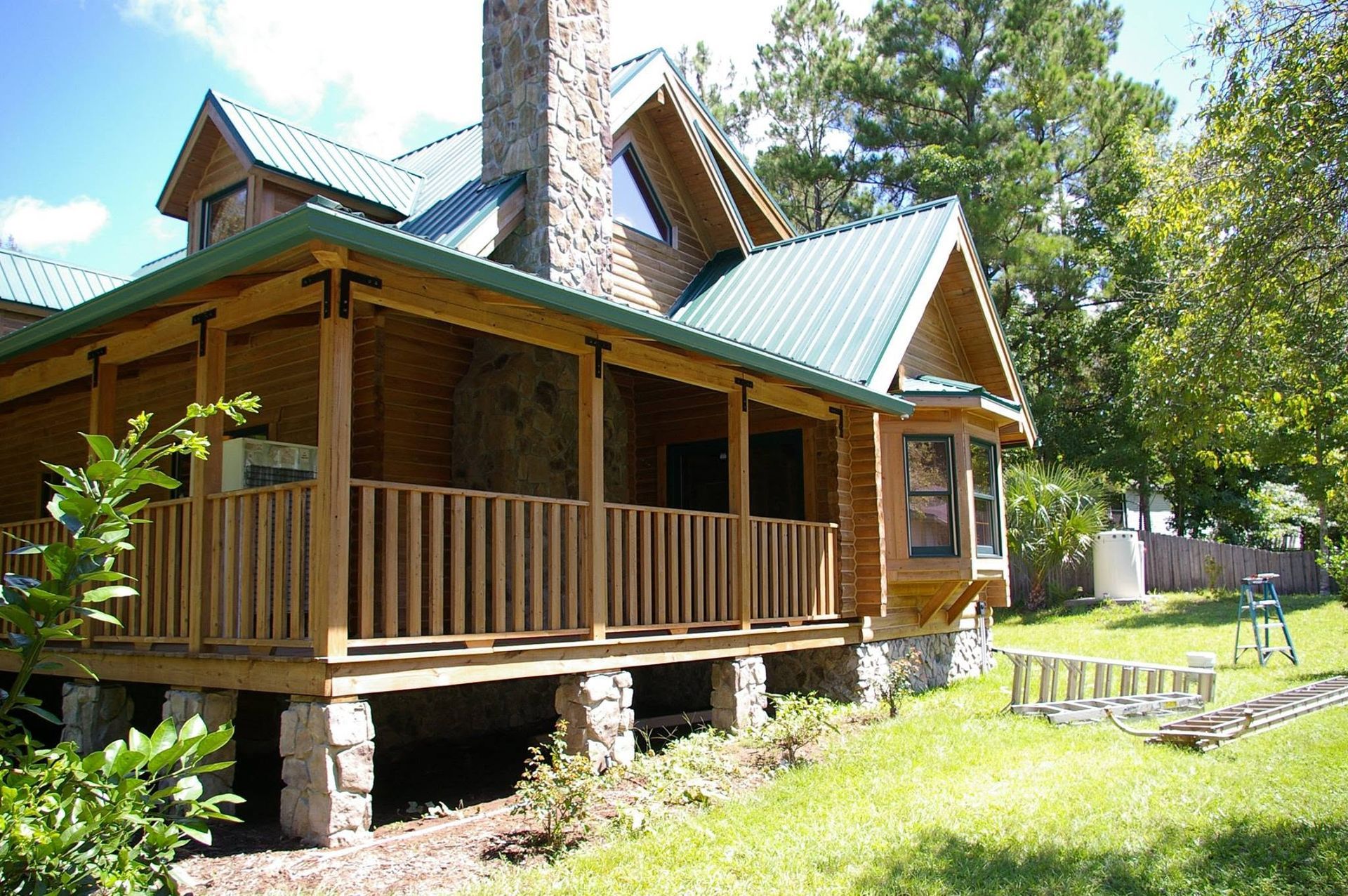 Rustic wooden cabin with green roof and porch in a sunny wooded yard
