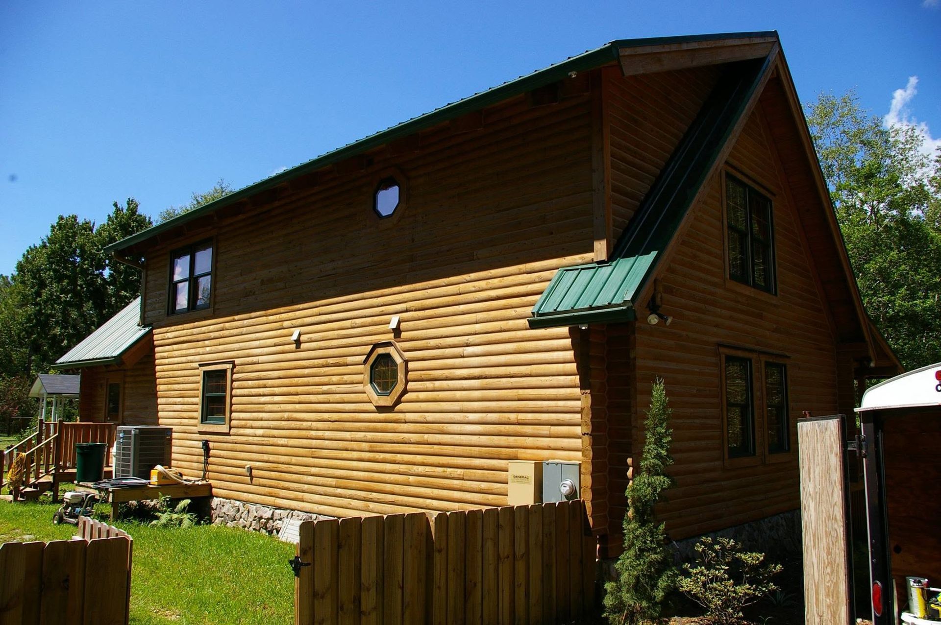 Wooden house with brown siding and a green roof in a sunny yard