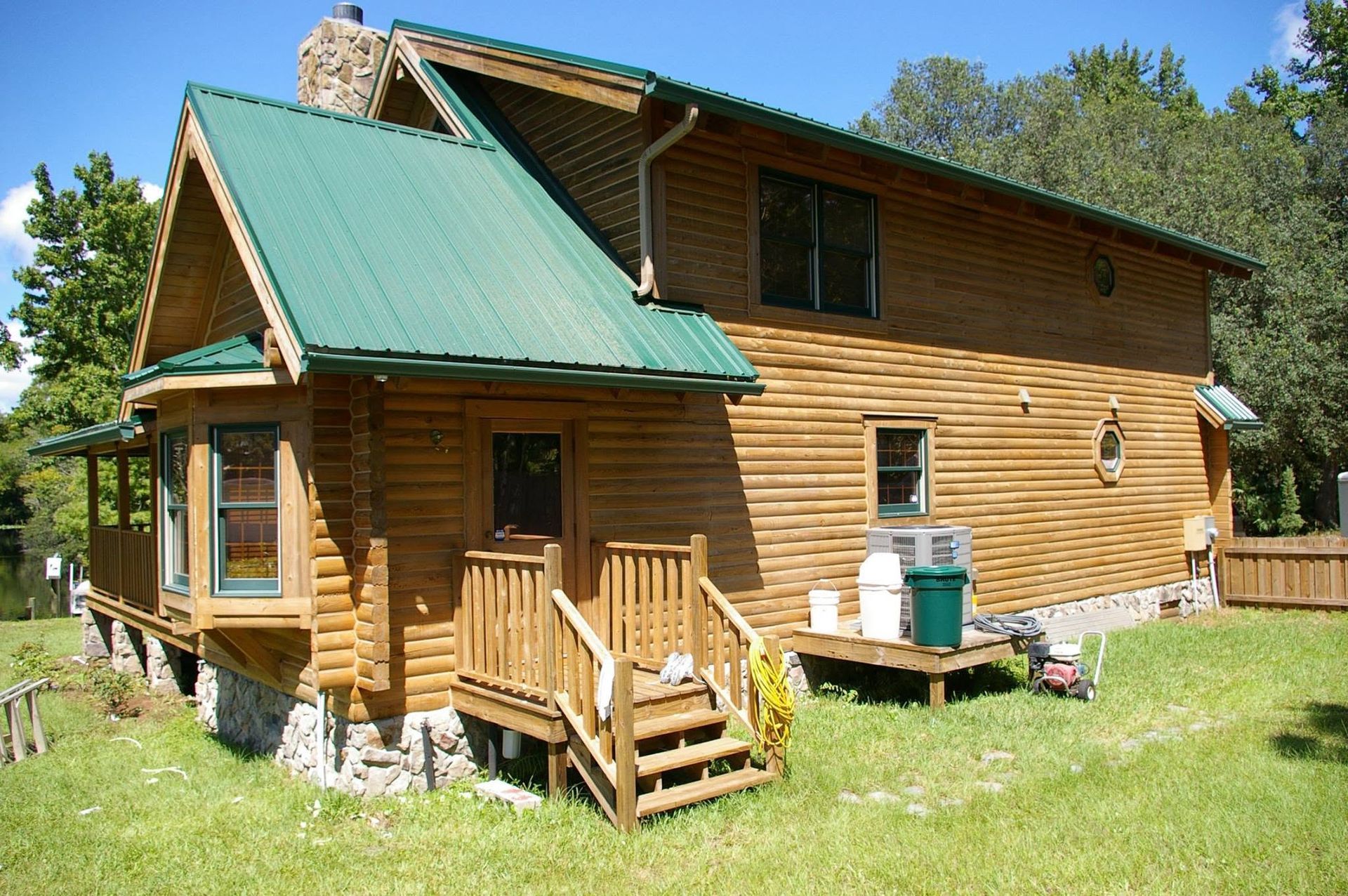 Wooden cabin with a green roof and small porch in a grassy yard under a clear blue sky