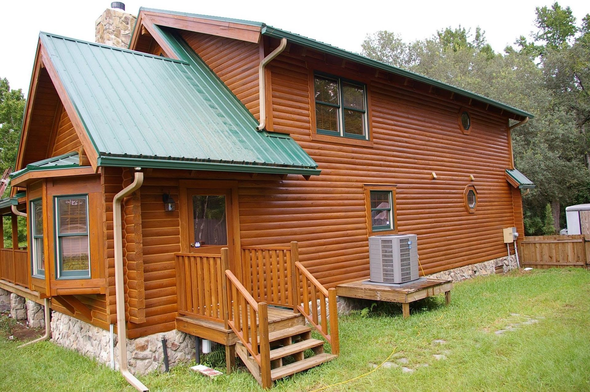 Wooden log cabin with green roof and front porch in a grassy yard