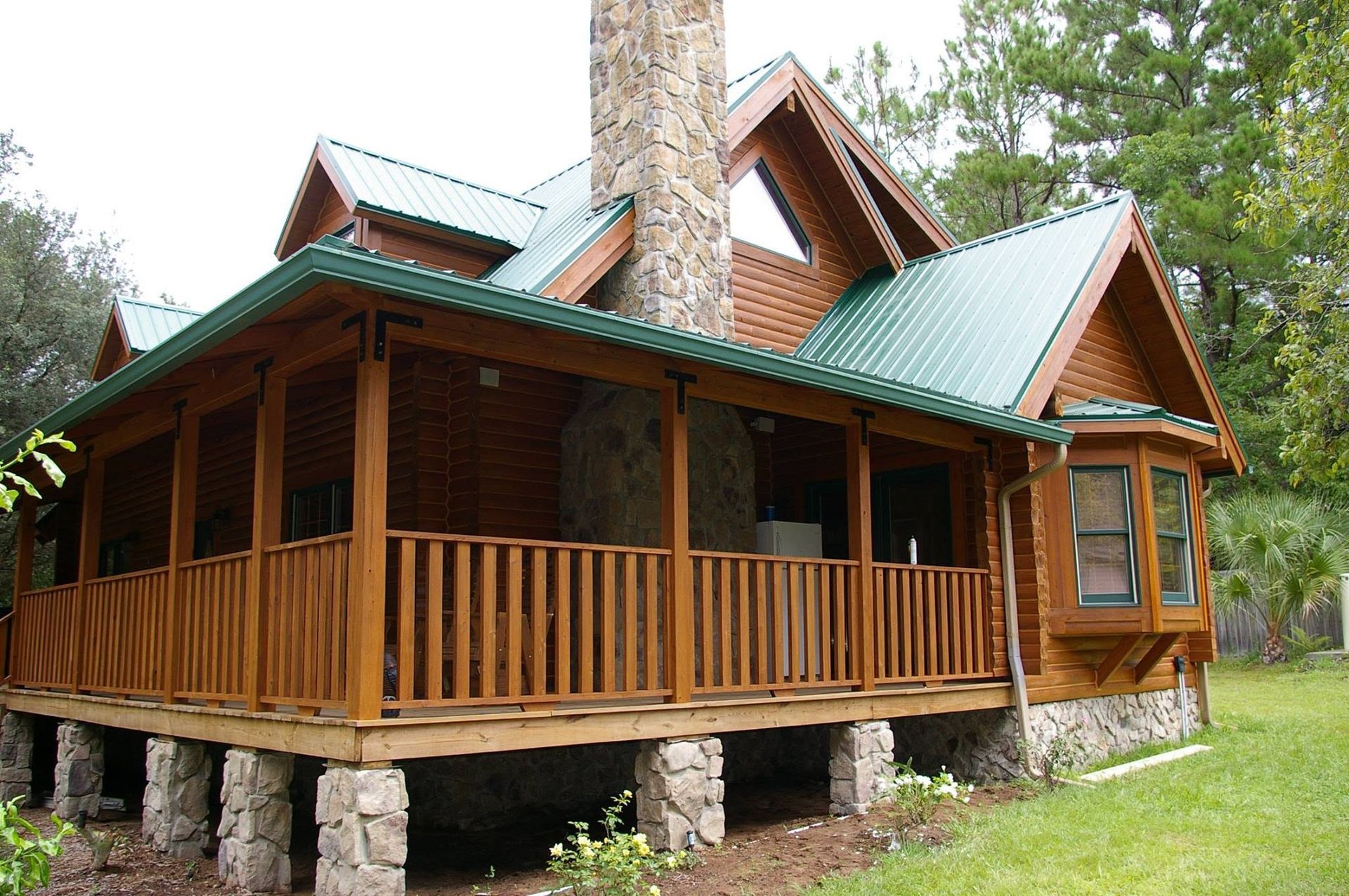 Rustic log cabin with green metal roof and wooden porch in a wooded setting