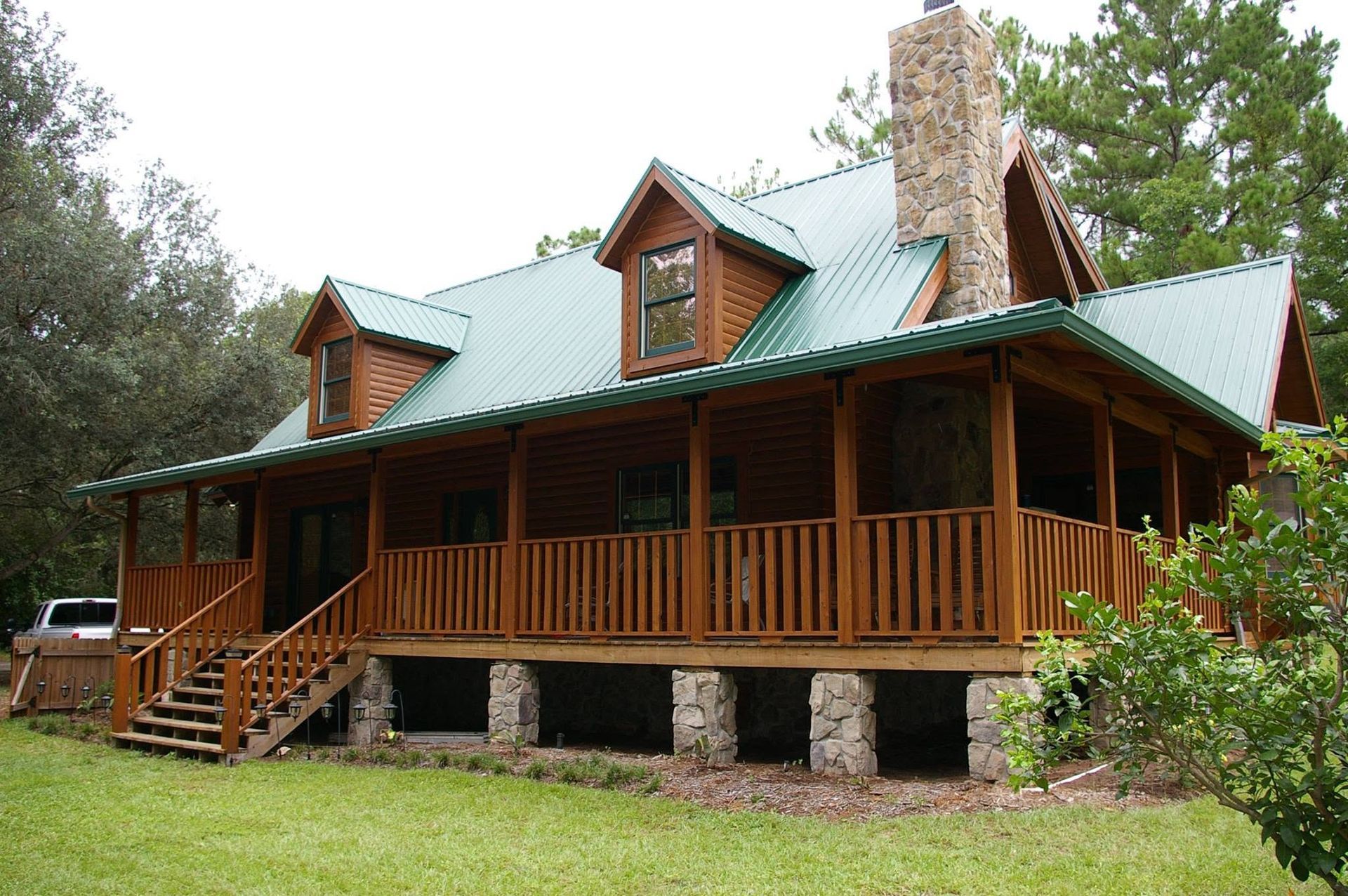 Rustic log cabin with green metal roof and wraparound porch in a wooded yard
