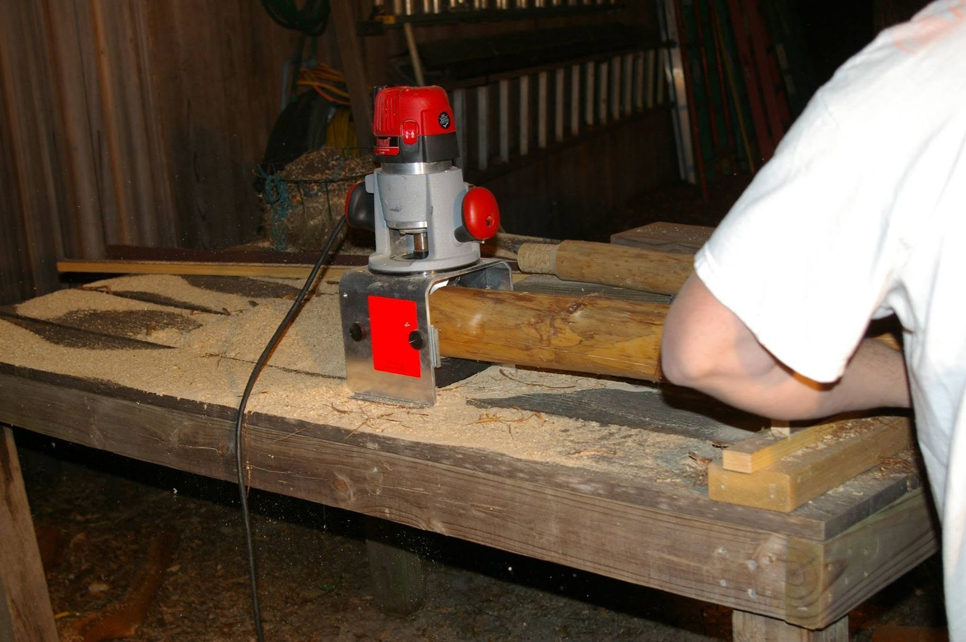 Router cutting wood on a workbench, with a person standing nearby in a workshop