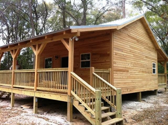 Wooden cabin with a covered porch and steps, set among trees in a wooded area.