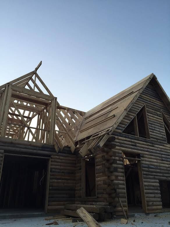 Partially built wooden log cabin with exposed roof framing under a clear blue sky