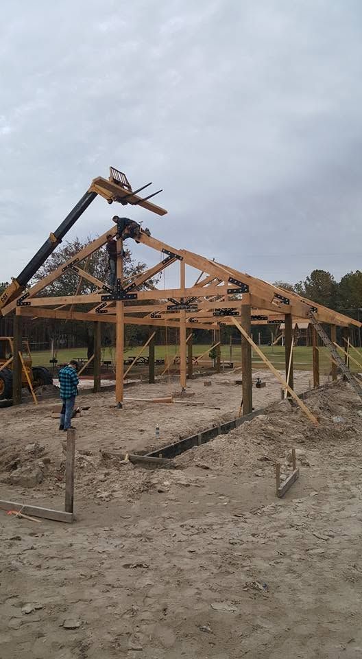 Construction site with a crane lifting roof trusses onto a wooden house frame under an overcast sky