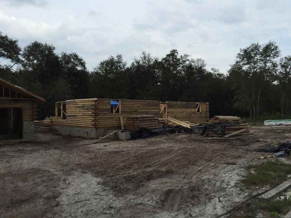 Stacked lumber and construction materials on a muddy site with trees in the background