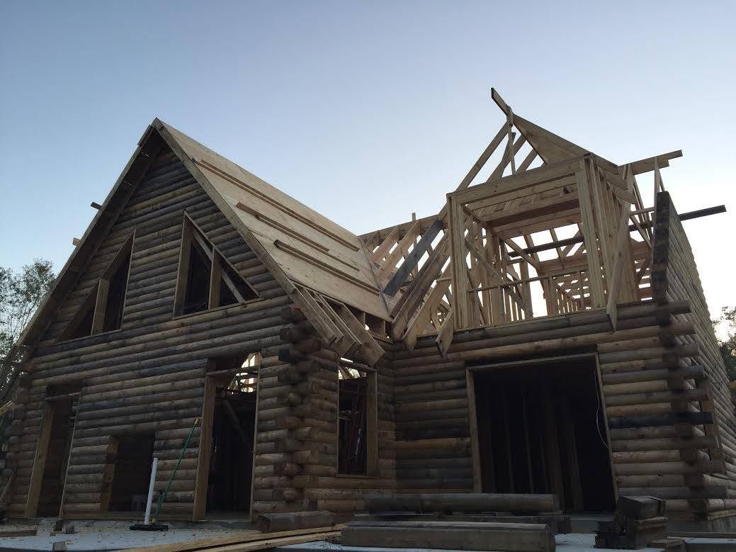 Partially built wooden log cabin with exposed roof framing under a cloudy sky