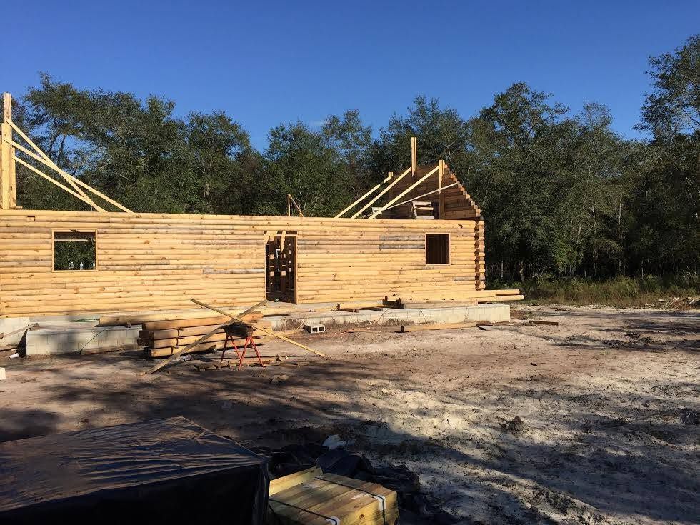 Partially built wooden house frame on a cleared lot under a blue sky