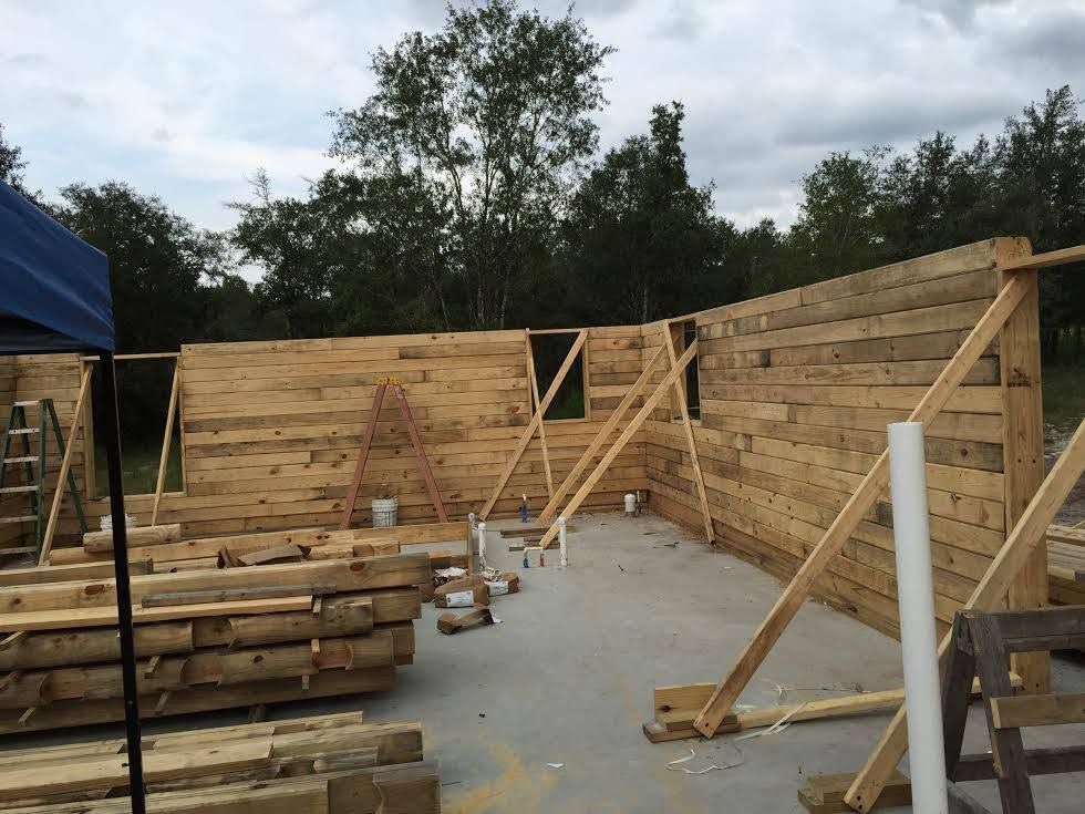 Partially built wooden structure with wall framing and stacked lumber in an outdoor worksite