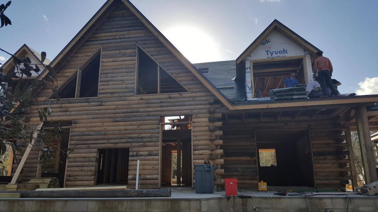 Rustic log cabin exterior with stone trim and large windows under a blue sky