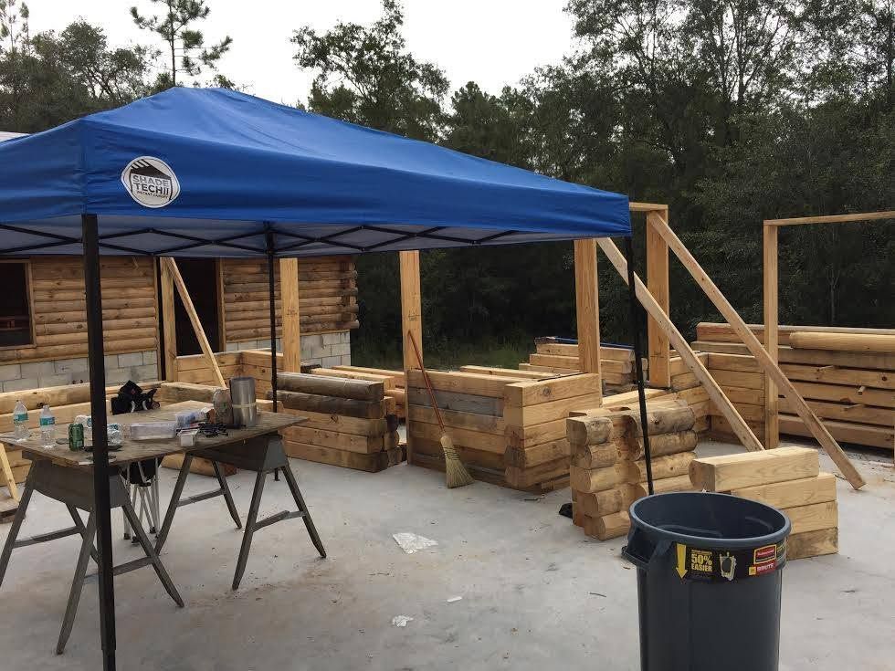 Blue canopy tent over lumber stacks and worktables at an outdoor construction site