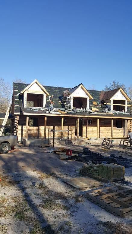 Partially built house with dormer windows, ladder, and construction materials under a clear blue sky