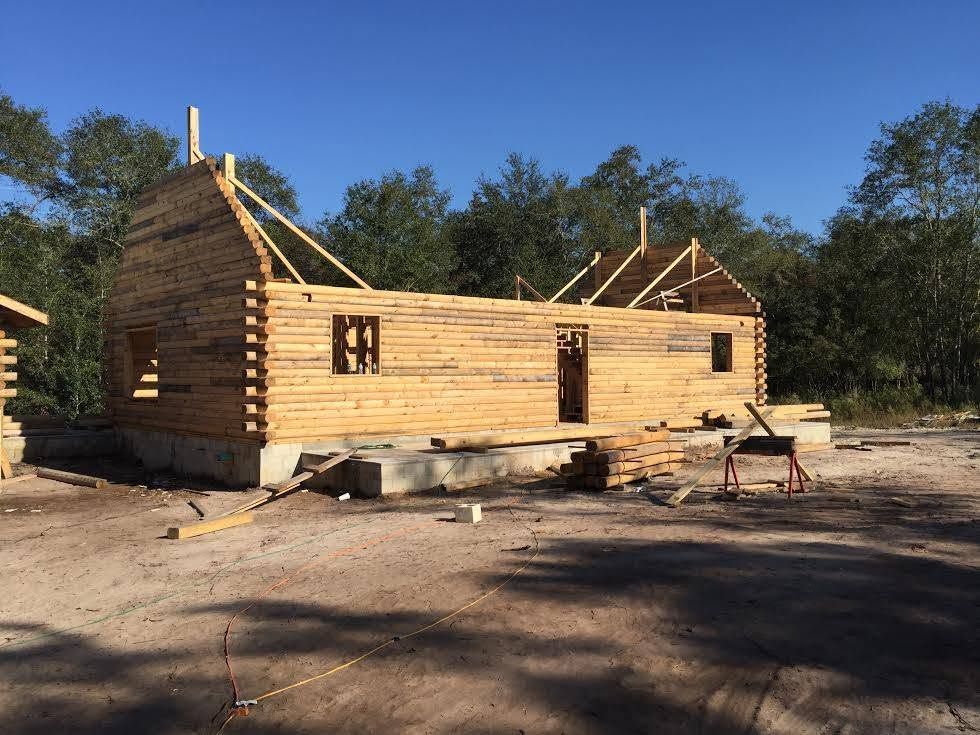 Partially built log cabin under construction in a wooded clearing with blue sky