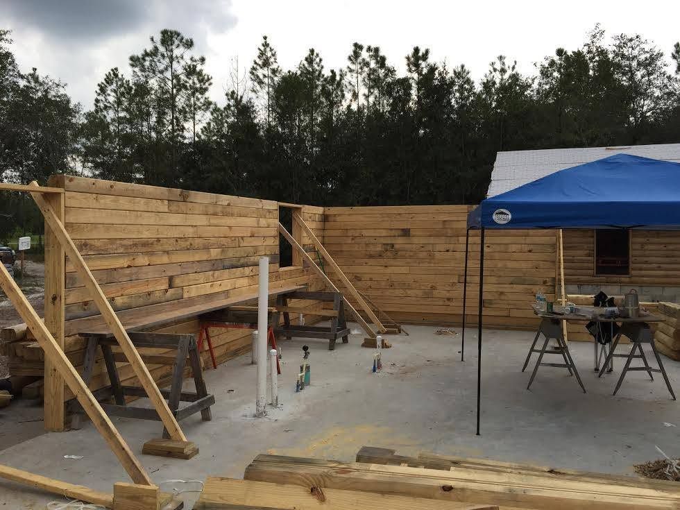 Wooden wall framing under construction beside a blue canopy on a concrete slab