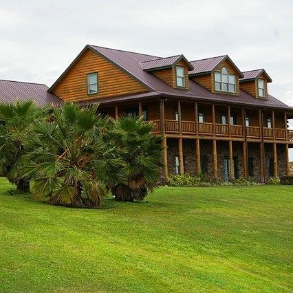 Rustic wooden lodge with wraparound porch and dormer windows on a green lawn