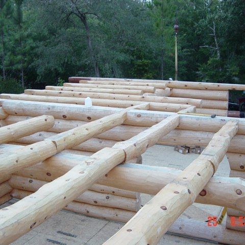 Stacked log beams laid out for a wooden cabin frame in a forest clearing