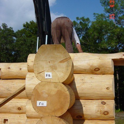 Stacked logs with a person climbing over them outdoors under a blue sky