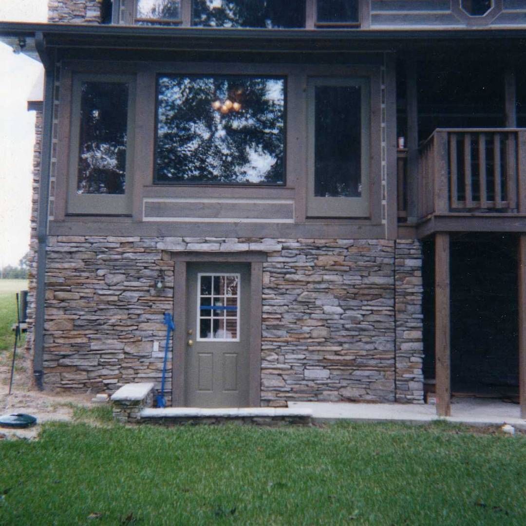 Two-story stone house exterior with a central door, large window, and small balcony on the right