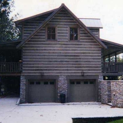 Wooden house with two garage doors and upper windows, viewed from the front in a snowy driveway