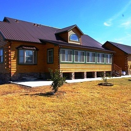 Log cabin-style house with a brown roof and yellow siding on a sunny day