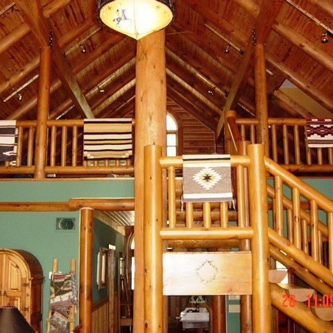 Rustic wooden cabin loft with log beams, railing, stairs, and hanging light fixture