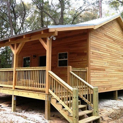 Wooden cabin with a front porch, railing, and steps in a wooded setting