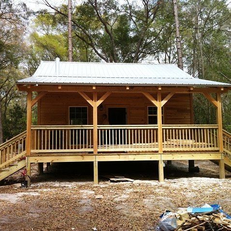 Wooden cabin porch with metal roof, front steps, and trees in a wooded clearing