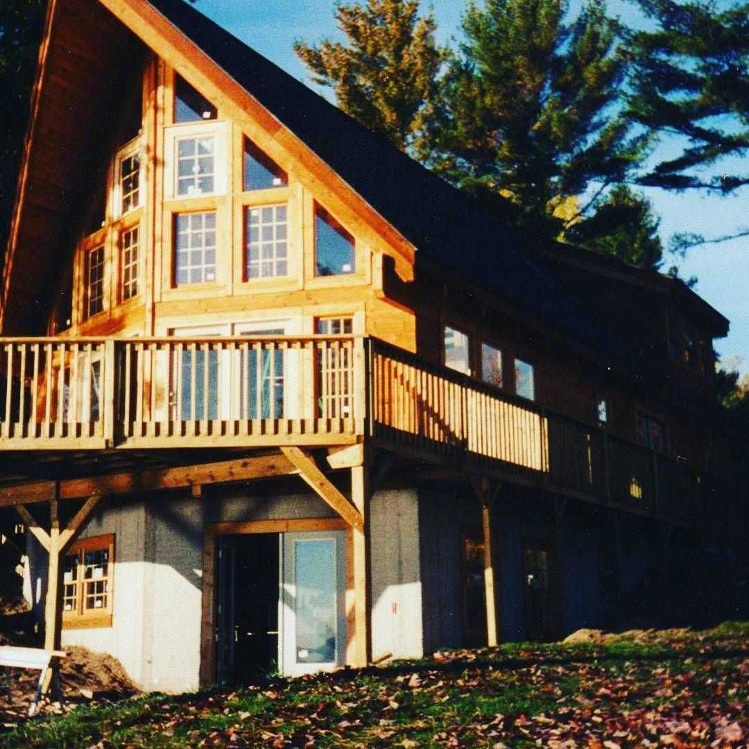 Wooden chalet-style house with large windows and a balcony, lit by warm sunlight among trees.