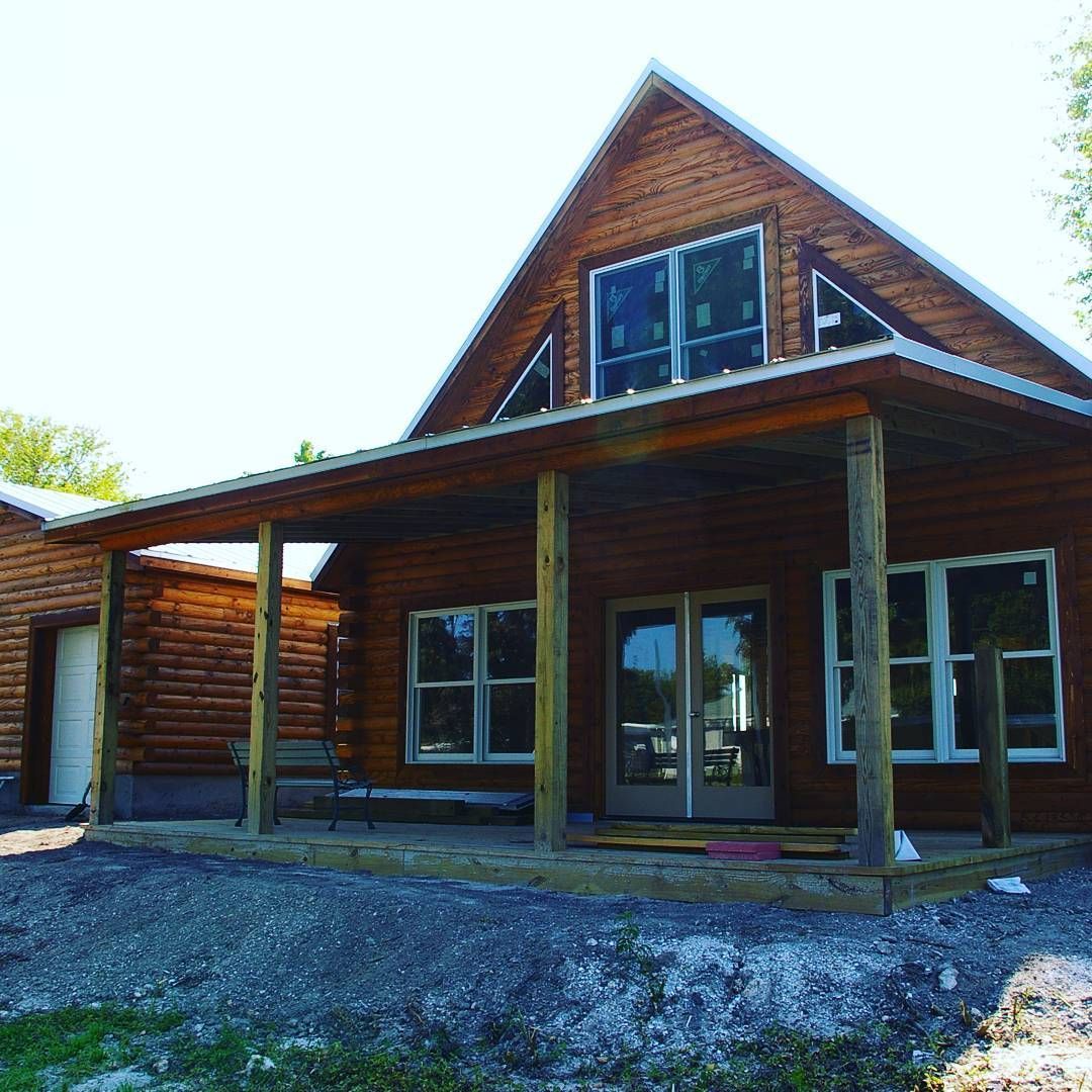 Rustic wooden cabin with porch and gravel driveway under a bright sky