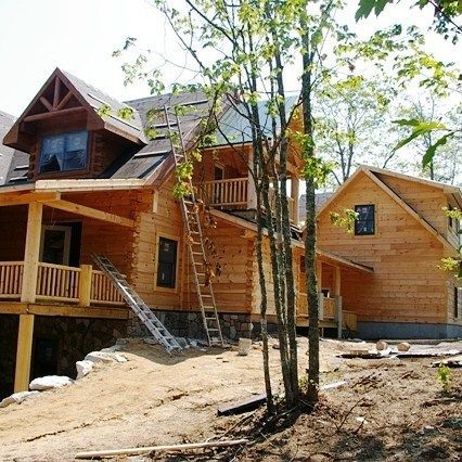 Wooden house under construction with ladders, trees, and a dirt yard