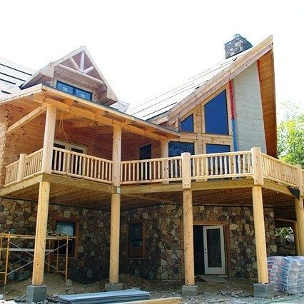 Wooden mountain-style house with stone base, balconies, and a steep roof under construction