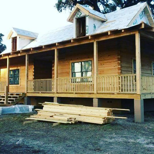 Wooden cabin porch with stacked lumber in front and a metal roof, under construction.