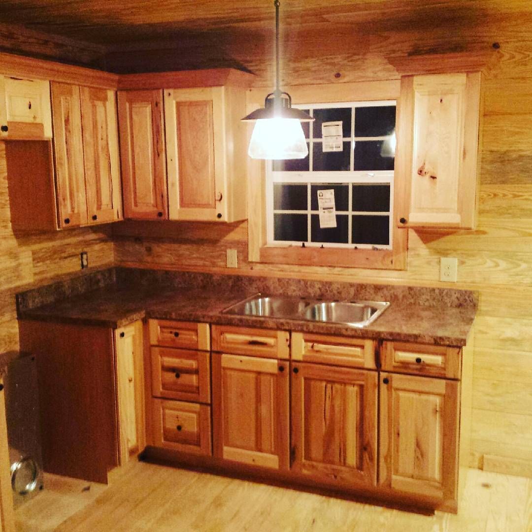 Warm wood kitchen with cabinets, granite counters, sink, and a hanging light over a window.