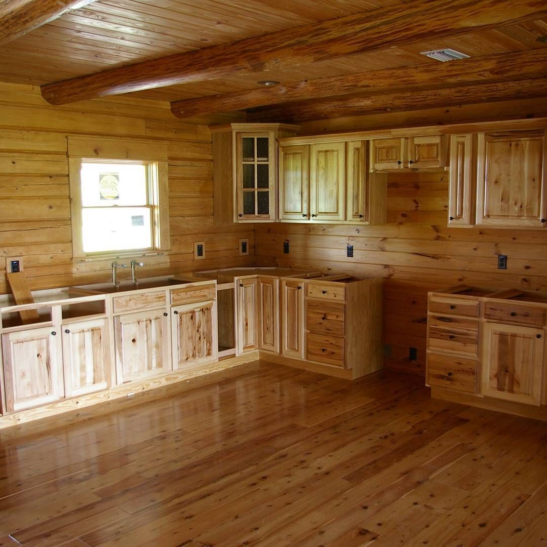 Empty rustic wooden kitchen with unfinished cabinets, wood-paneled walls, and a hardwood floor