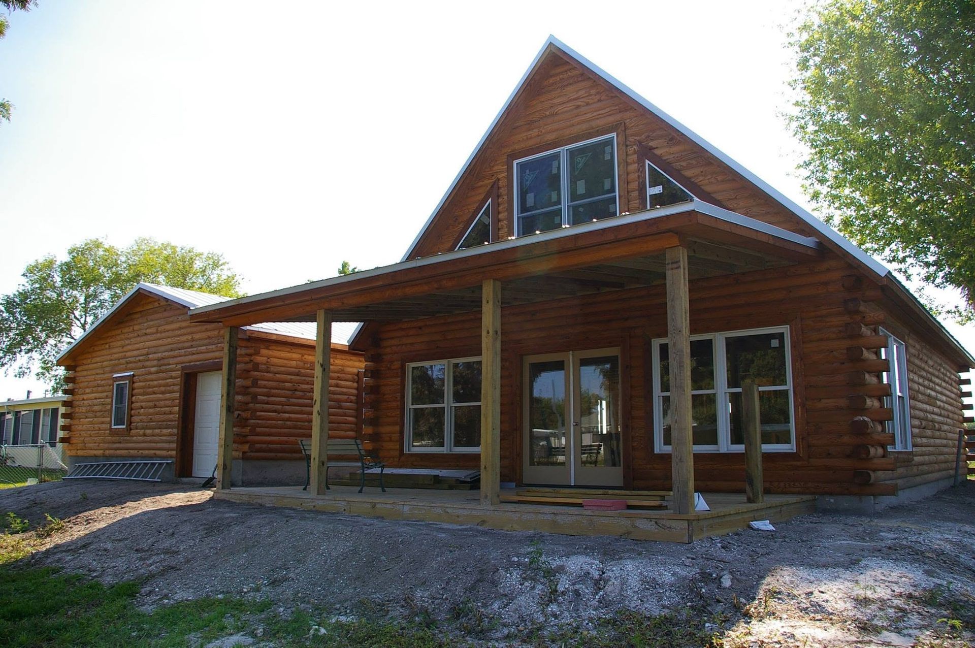 Rustic log cabin with a covered porch and gravel driveway, set among trees in daylight