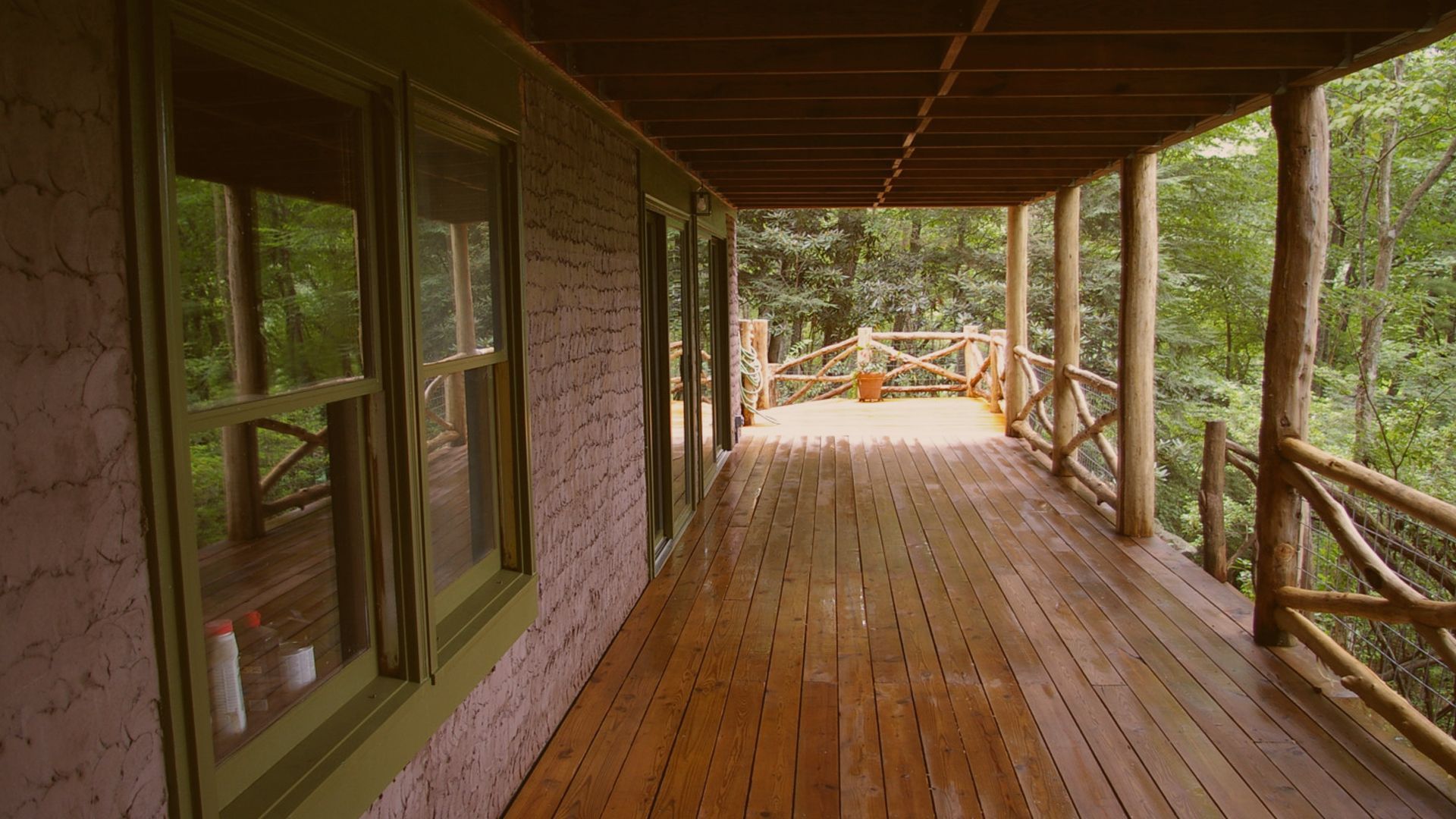 Wooden porch with railings overlooking a wooded area, with doors along the left side.
