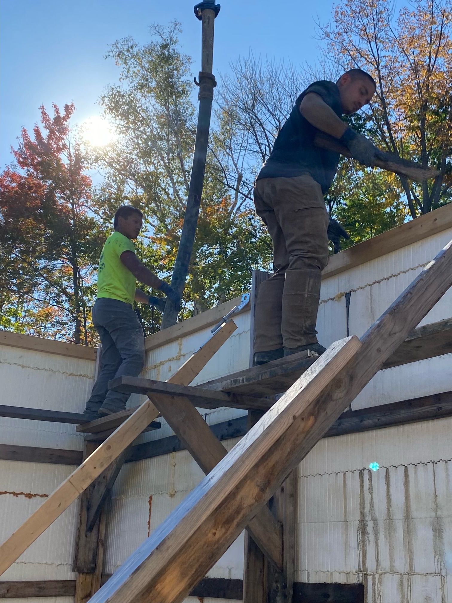 Two workers standing on wooden roof framing, installing a rooftop structure outdoors.