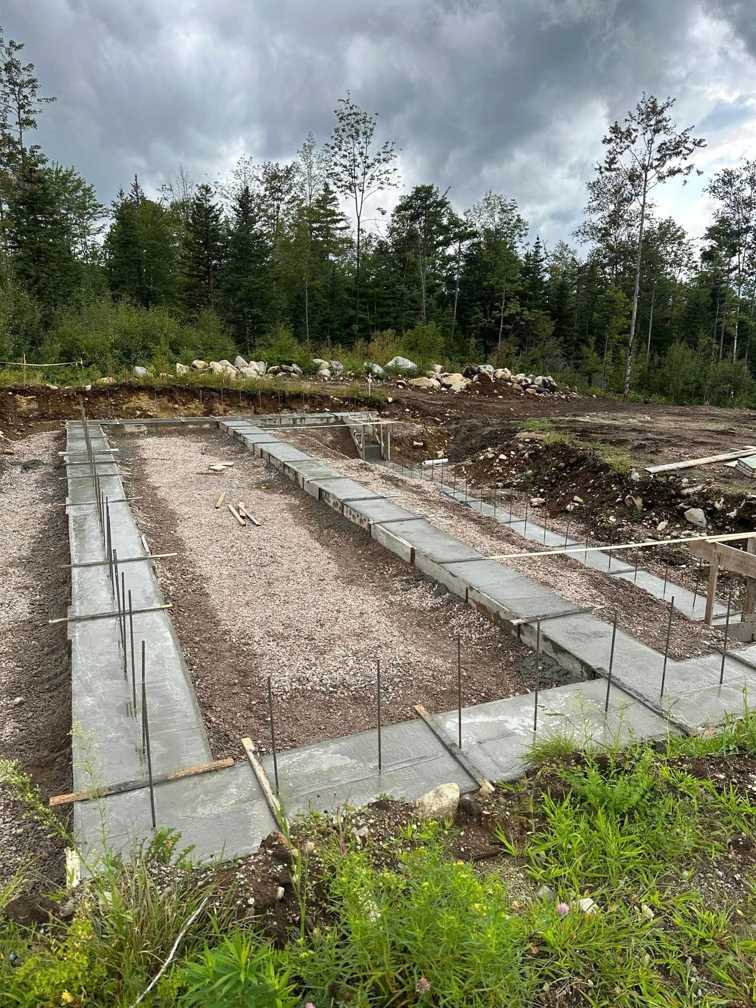 Stone-lined rectangular grave plot in an outdoor cemetery, surrounded by grass and trees under a cloudy sky