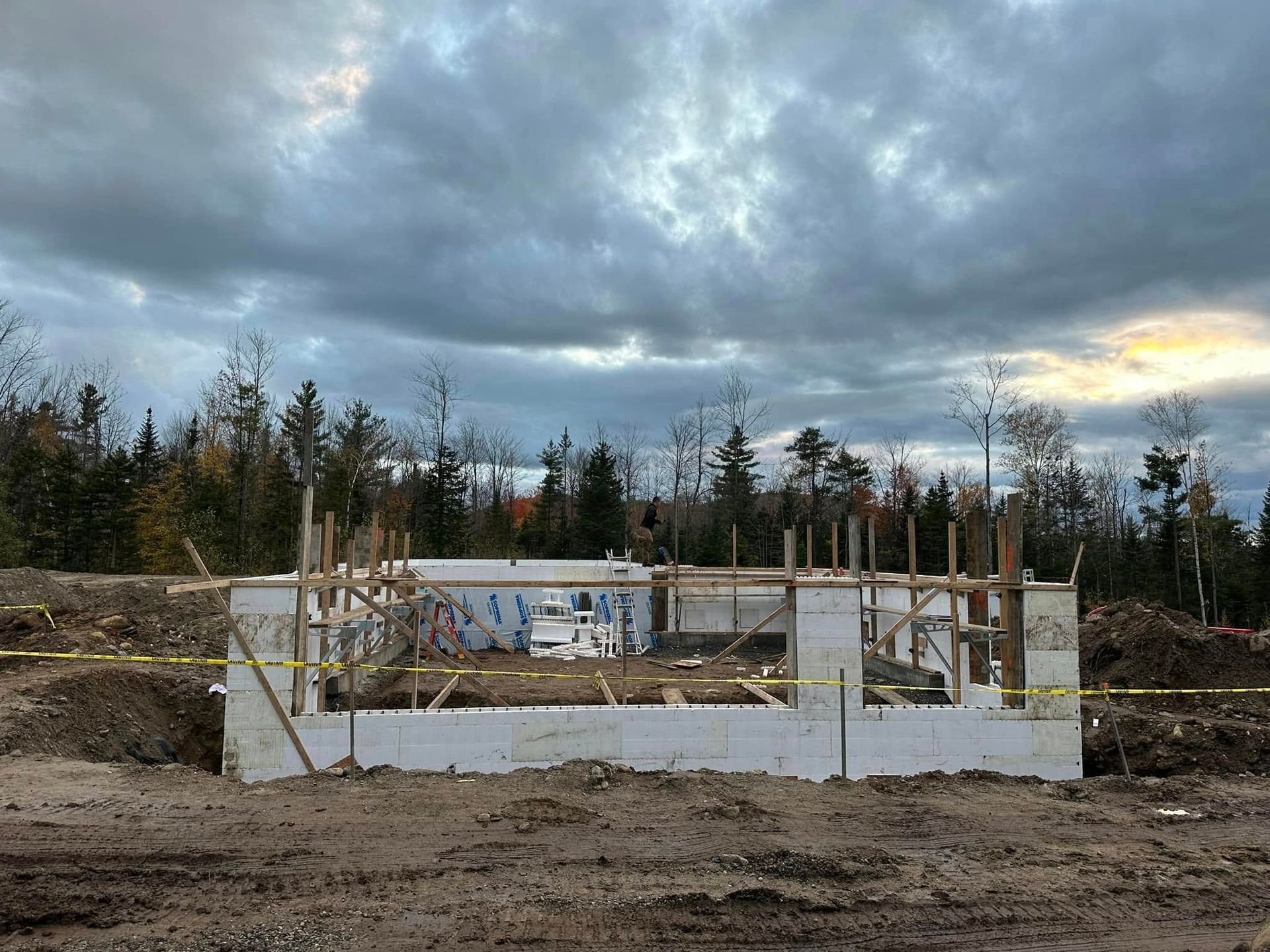 Concrete foundation under construction in a muddy field, with wooden forms and a cloudy sky.