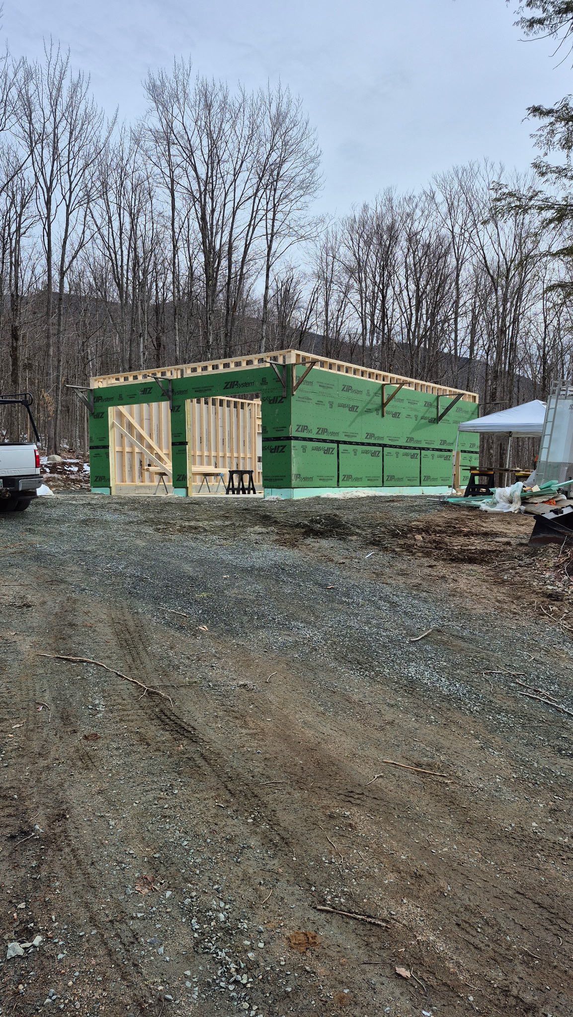 Green house under construction on a gravel driveway in a wooded area