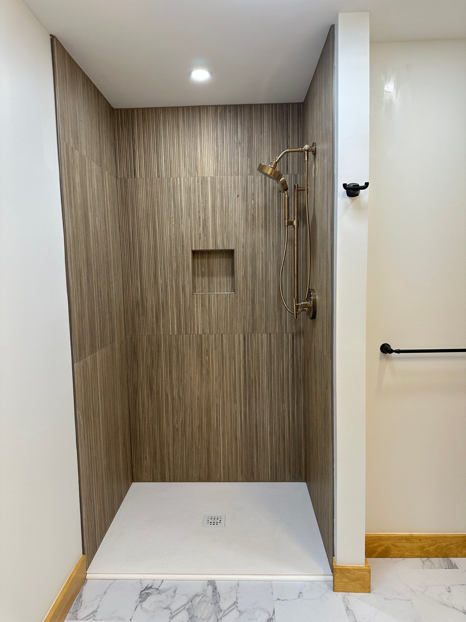 Accessible shower stall with wood-look tile walls, grab bars, a bench, and a low curb entrance