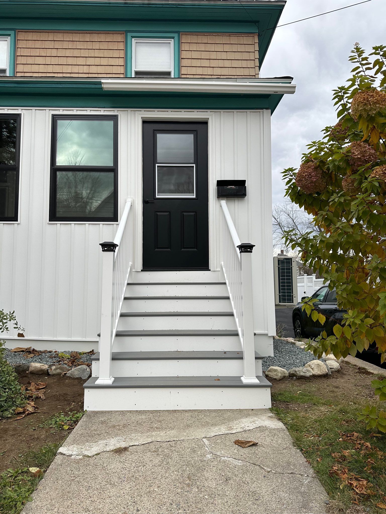 Front entrance of a house with white siding, black door, steps, and a small mailbox.