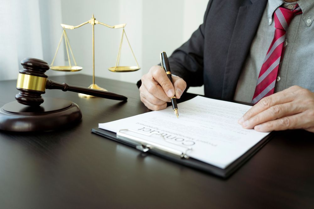 A Person in a Suit Signing a Contract With a Gavel and Scales of Justice — Umbrella Legal in Wyong, NSW